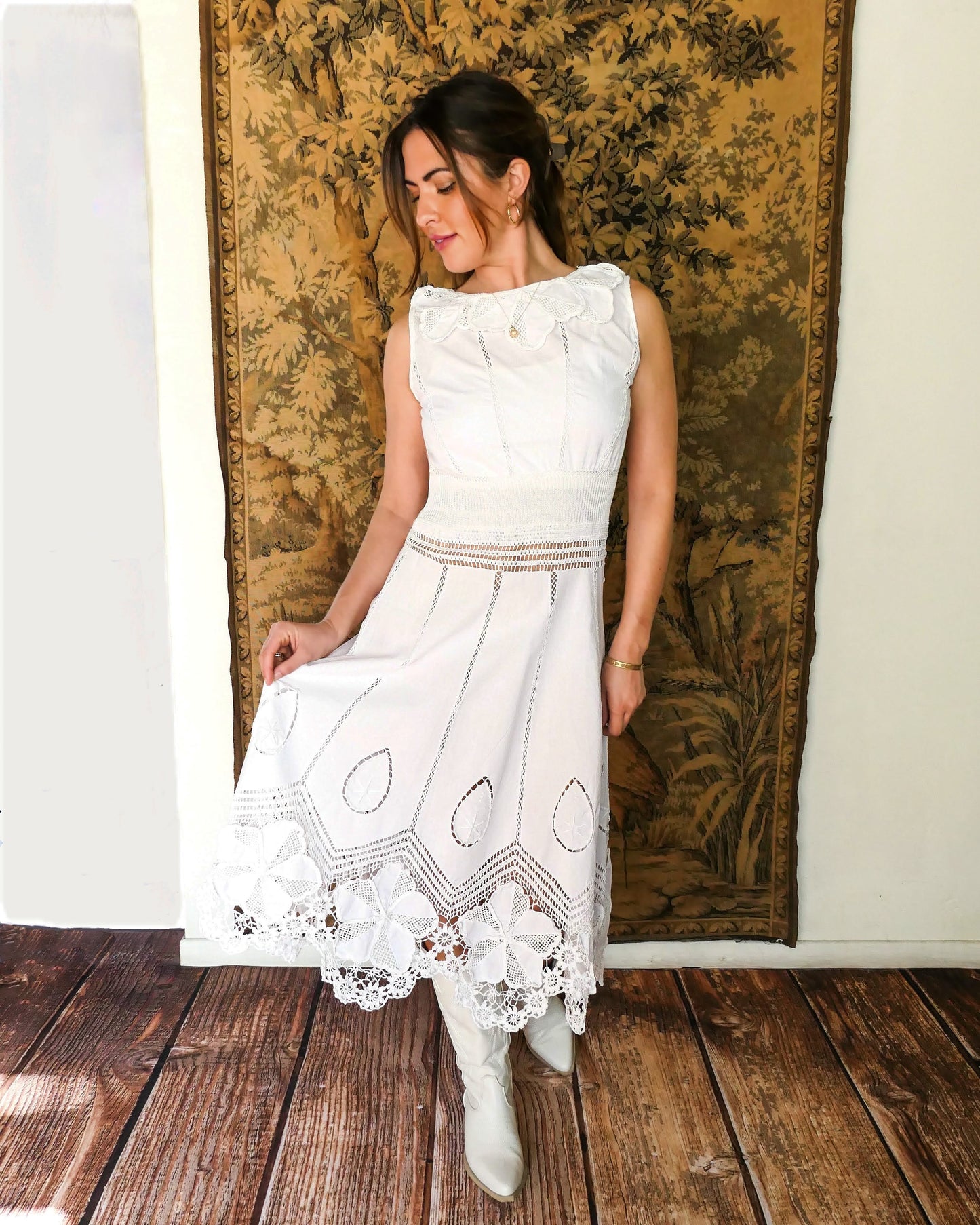 A white cotton midi dress with whimsical crochet and embroidered flowers at the hem and collar, and teardrop shaped eyelet detail on the skirt. Stretchable ribbed knit fabric around the waist adds contour to the dress. By Lim's Vintage.
