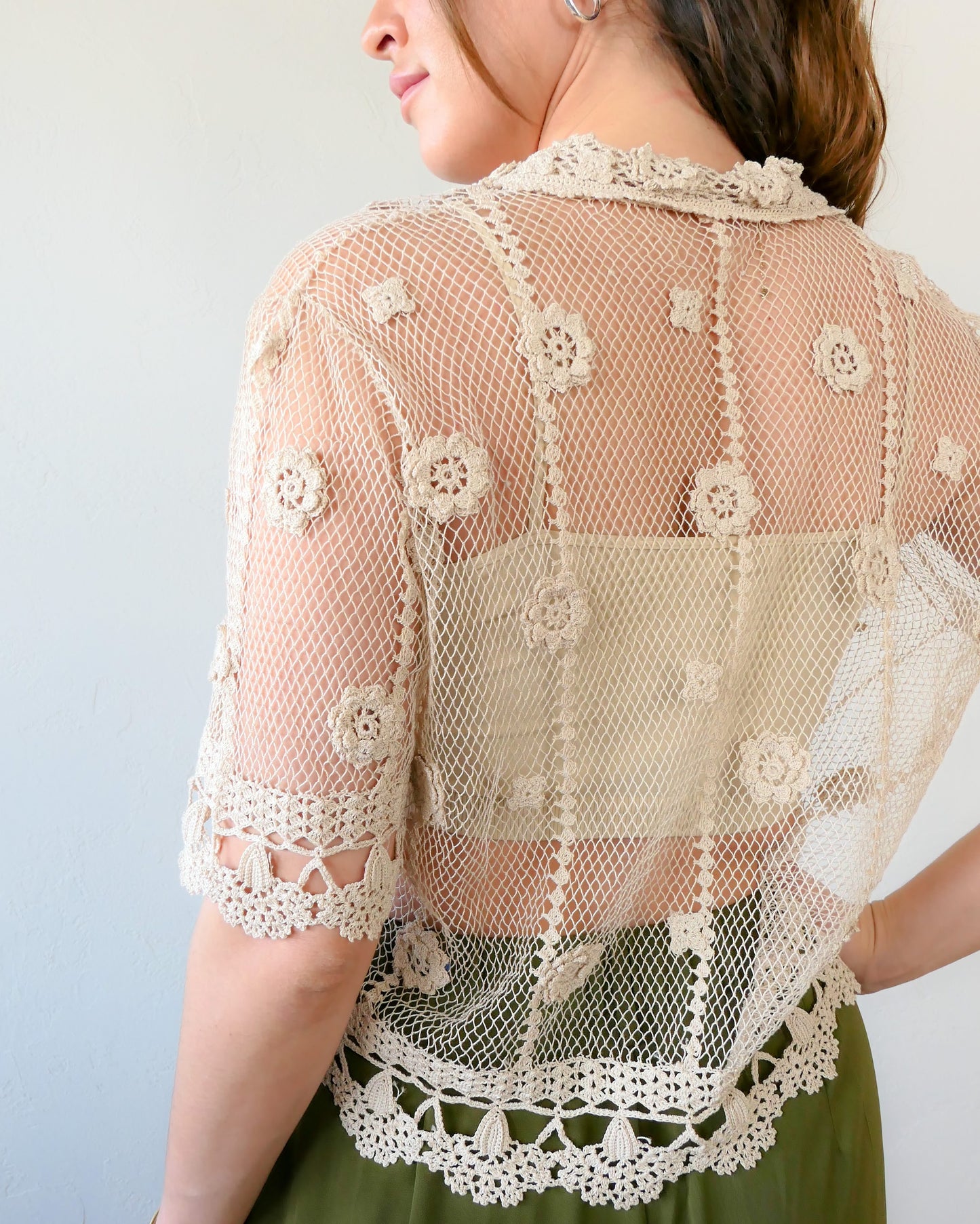 Back view of top. One of the last of our original Lim's hand crocheted half sleeve button down tops in Natural from the 1990s, this versatile, lightweight, sheer top with a notched collar and floral motif design is sure to catch a few eyes. Relaxed, easy fit with dainty, hand crocheted flowers throughout and a scalloped hem reminiscent of upside down carnations. Dress it up or down any way you like.