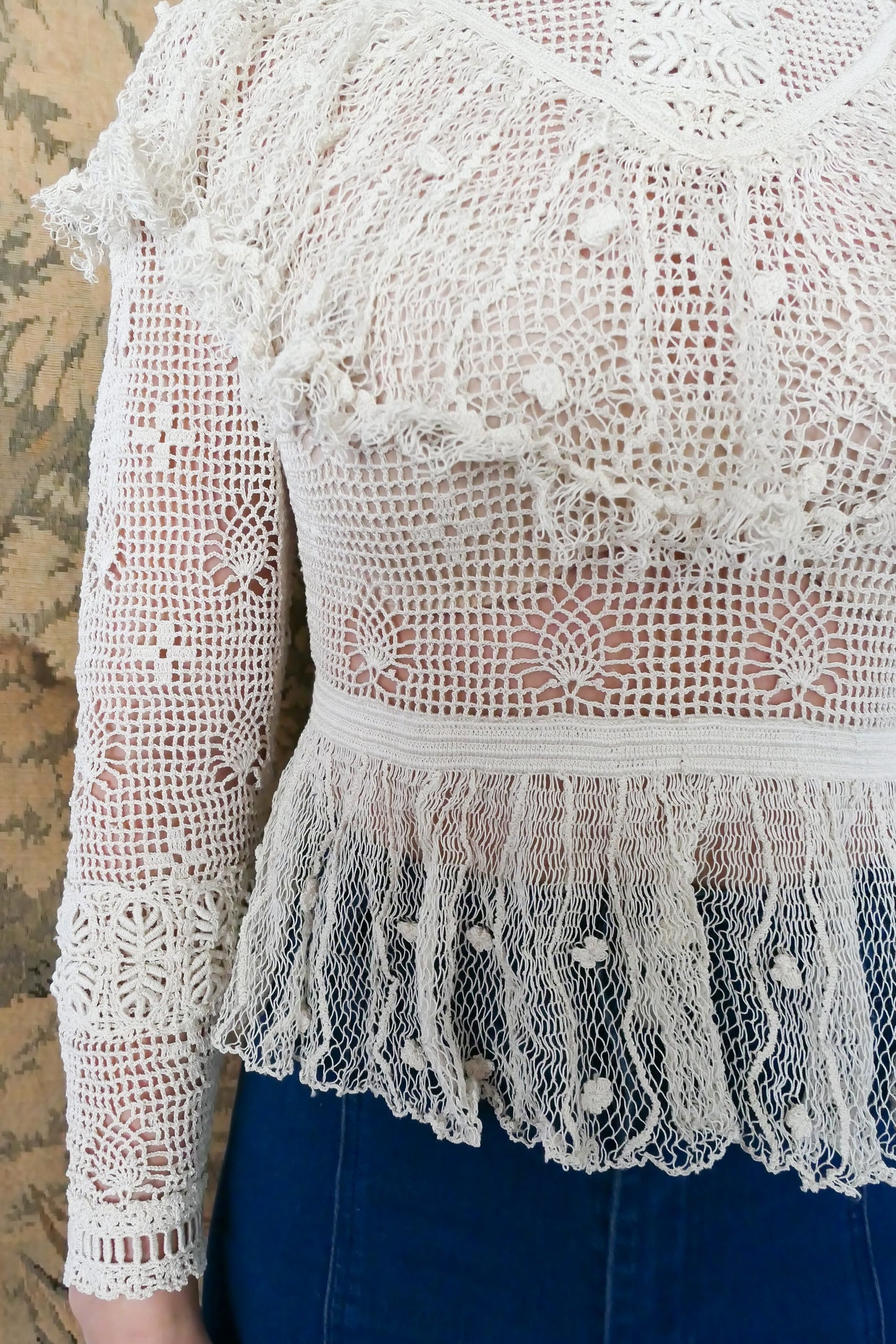 Closeup view of ruffled flared bottom hem of top made with sheer fishnet-like crochet material.. Waist is fitted.