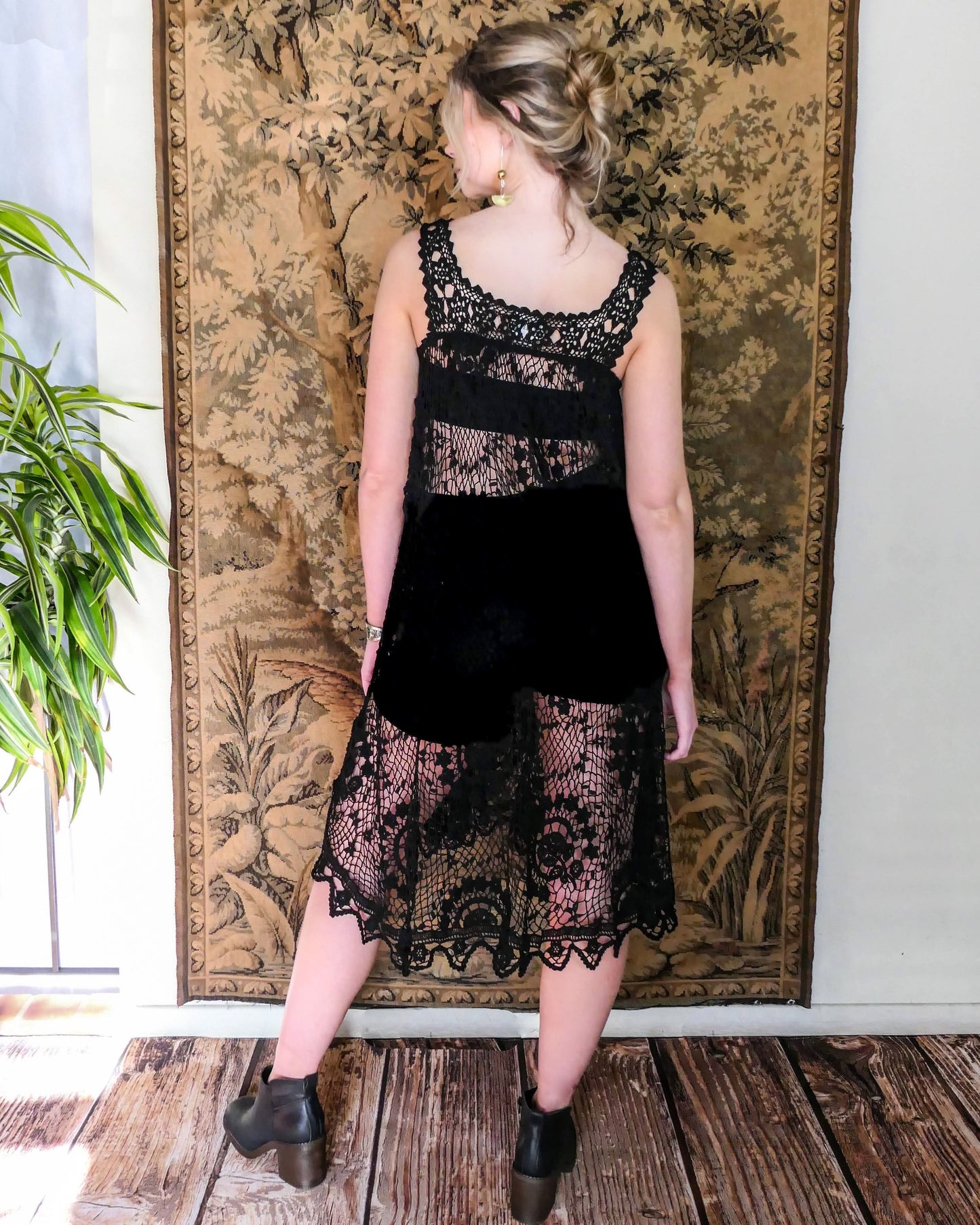 Back view of model wearing the dress. A sleeveless babydoll dress made from our Lim's Vintage original fishnet crochet fabric with a repeating floral themed design throughout. A versatile, comfortable, fun-to-twirl-around-in pullover dress that you can wear wherever you go. The area above the breast and under the armpits is elastic and stretchable, making the dress suitable for most sizes. Color: Black, Size: One size fits most