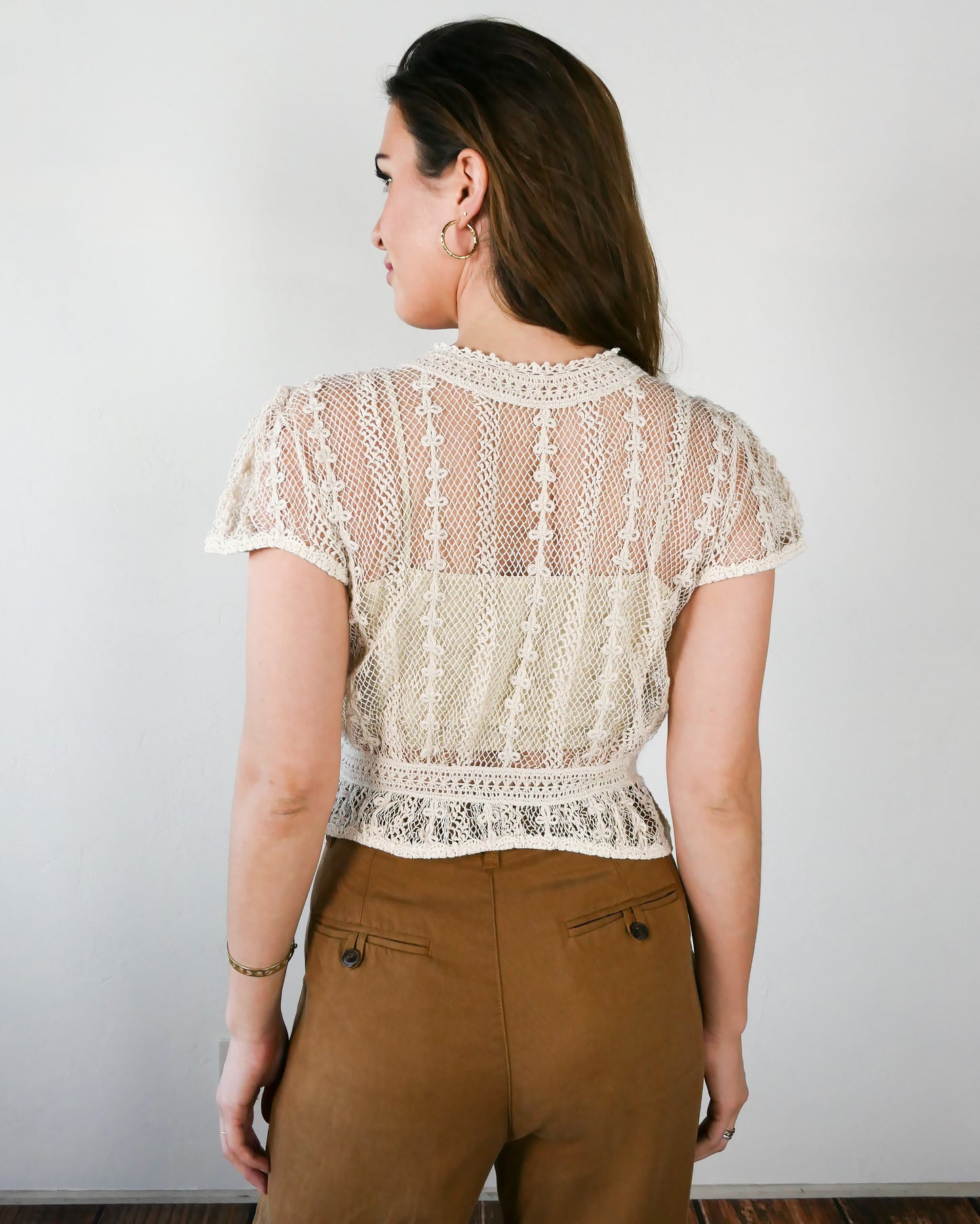 Back view of natural colored crochet top. A Lim's original vintage crochet piece from the 1980s, this top was hand crocheted with very fine threads to create a delicate, lightweight, and transparent feel. Puffed sleeves, a high waist, and flared hem lend the top a whimsical yet tailored look. The top is reversible and can be buttoned up the front or back. Natural color.