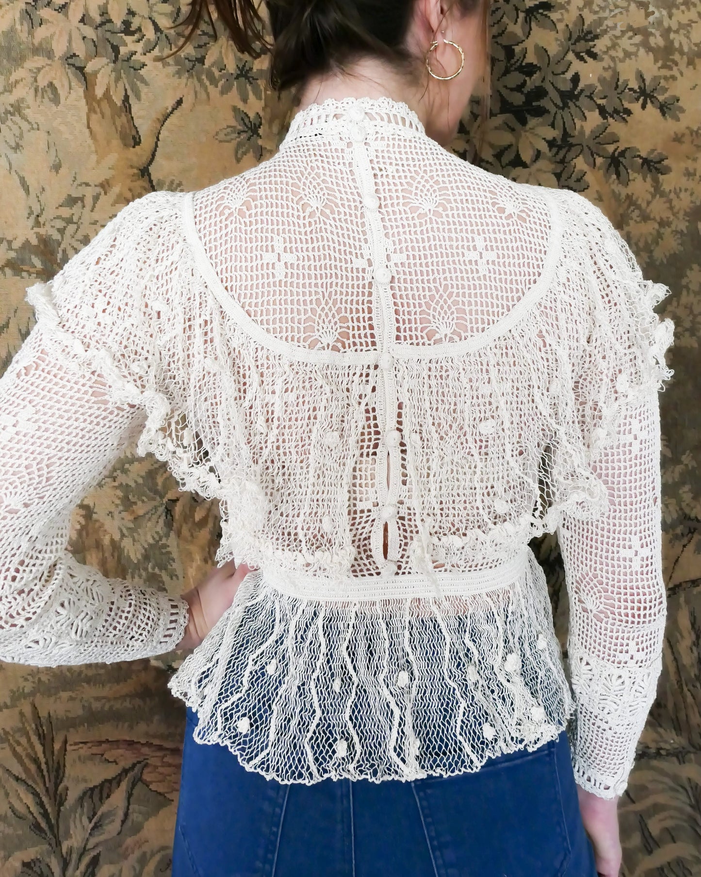 Back view of Lim's Victorian crochet long sleeve top in Natural. Lim's original crochet top from the 1980s. Slightly thicker threads were used to crochet the body of the top, and very fine threads give the ruffled parts a lightweight, feminine touch. High Victorian neckline, a beautiful, intricate trim on the sleeves and chest, and a fitted waist and flared hem to create a flattering silhouette. The top is reversible and can be worn with the buttons going down the front or back. T