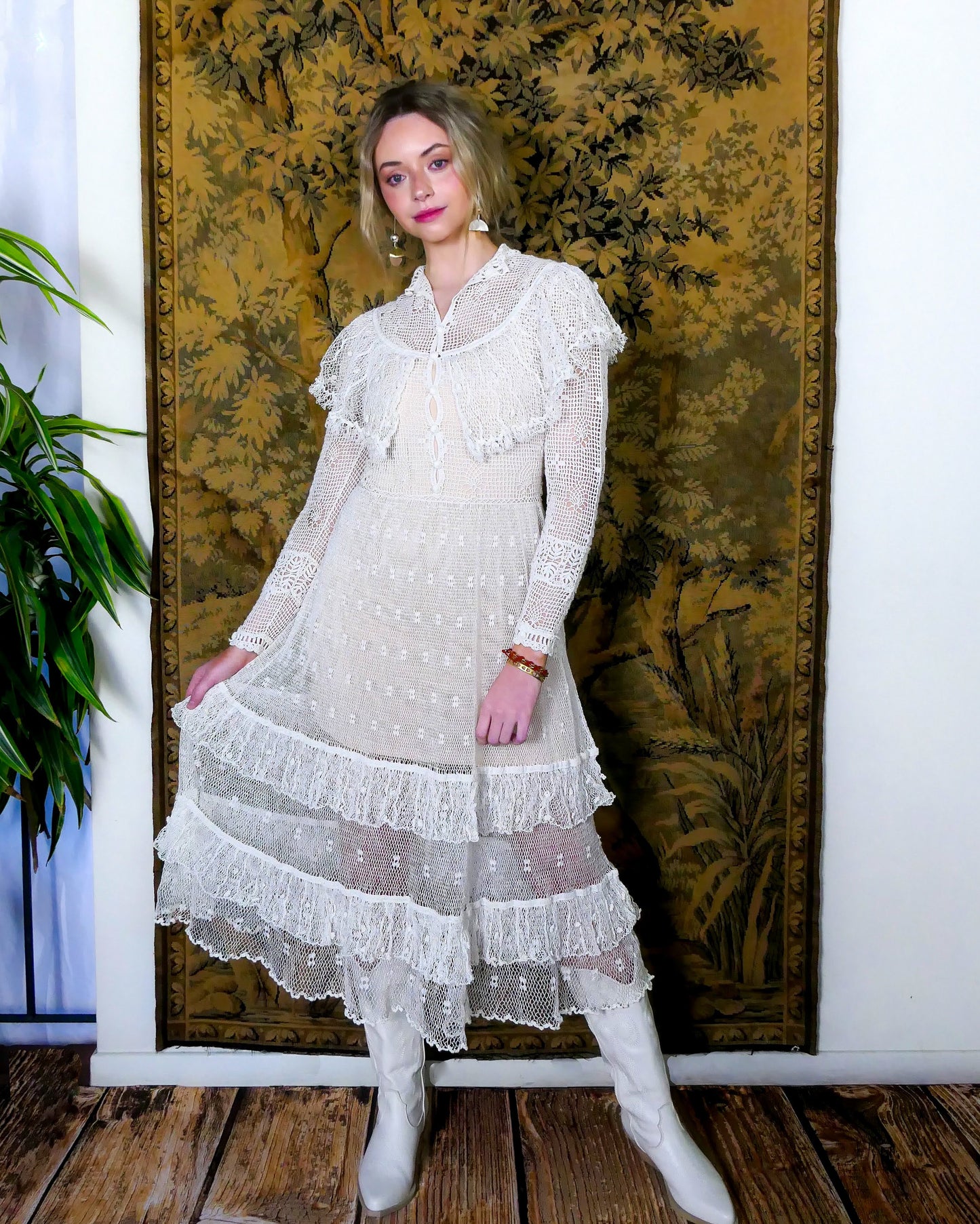 Lim's original hand crocheted maxi dress from the 1980s, worn by Jane Fonda and placed in a major fashion magazine ad. The dress is reversible and can be worn with the buttons going up the front or back of the dress. Ruffle trim along the chest covering the breast area, and two tiered ruffle hem at the bottom of the dress. Very sheer crochet dress, fitted at the waist, with a tie at the back. Detailed crochet emellishment on the forearm, sleeve hem, and neckline. Models is wearing white colored dress.