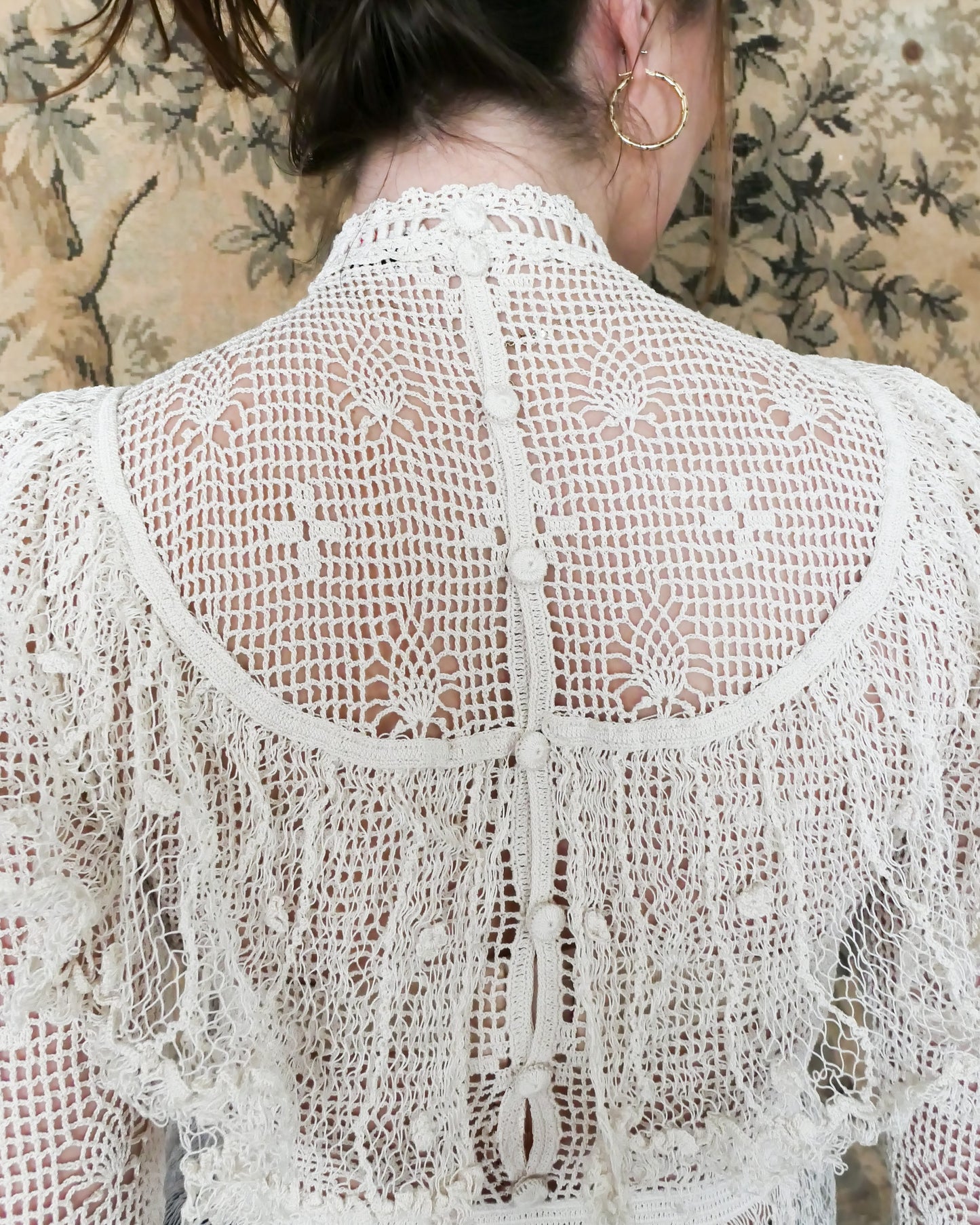 Closeup view of back of Lim's crochet top at neck and shoulders. High Victorian neckline, buttons up the back. Natural color.