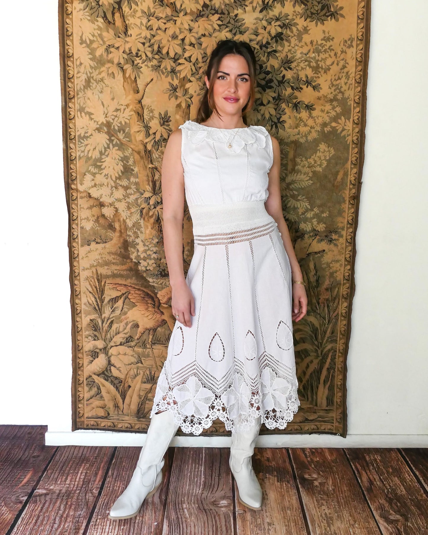 A white cotton midi dress with whimsical crochet and embroidered flowers at the hem and collar, and teardrop shaped eyelet detail on the skirt. Stretchable ribbed knit fabric around the waist adds contour to the dress. Made by Lim's Vintage.