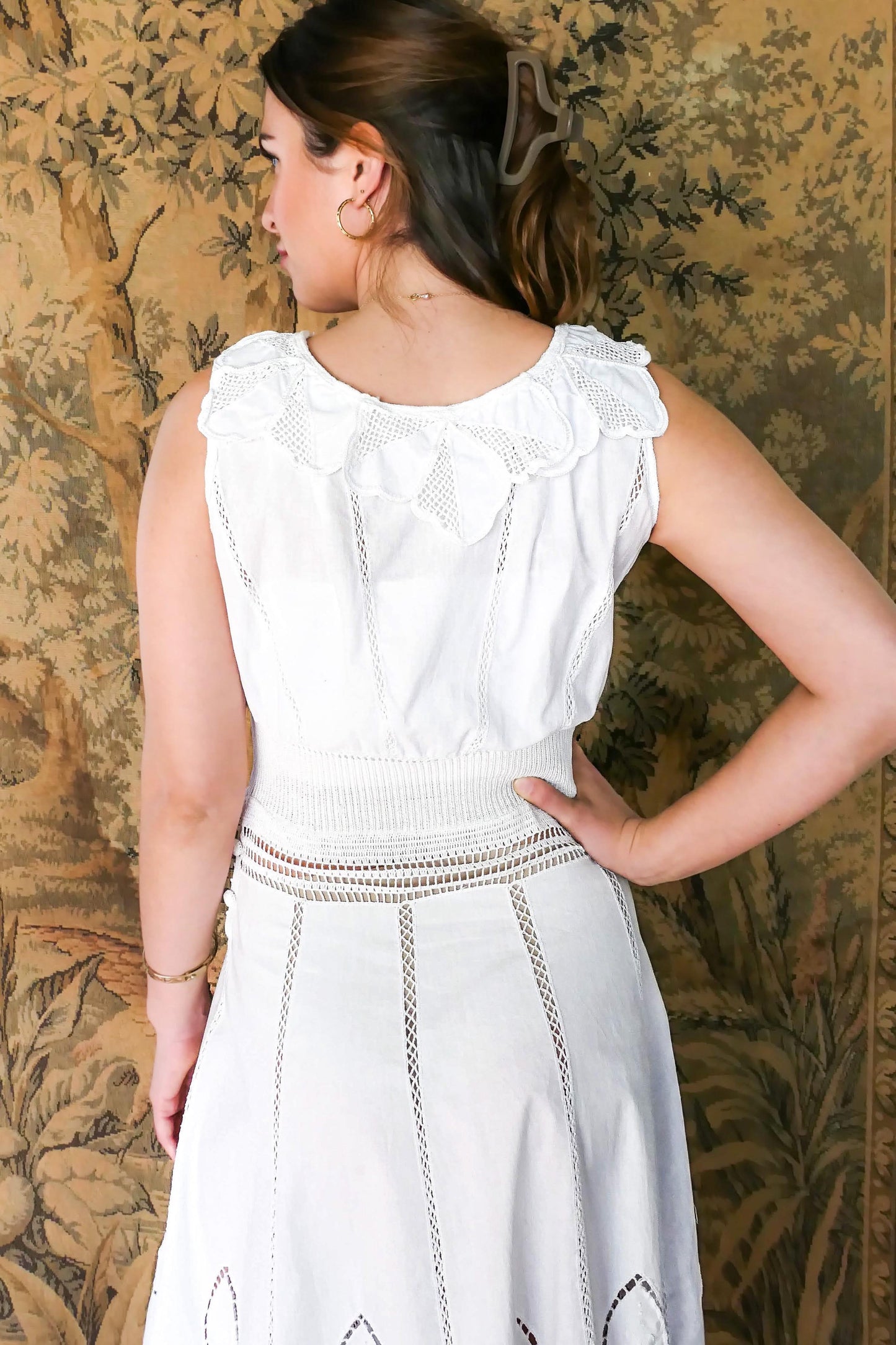 Closeup view of back of dress with floral inspired collar. A white cotton midi dress with whimsical crochet and embroidered flowers at the hem and collar, and teardrop shaped eyelet detail on the skirt. Stretchable ribbed knit fabric around the waist adds contour to the dress.