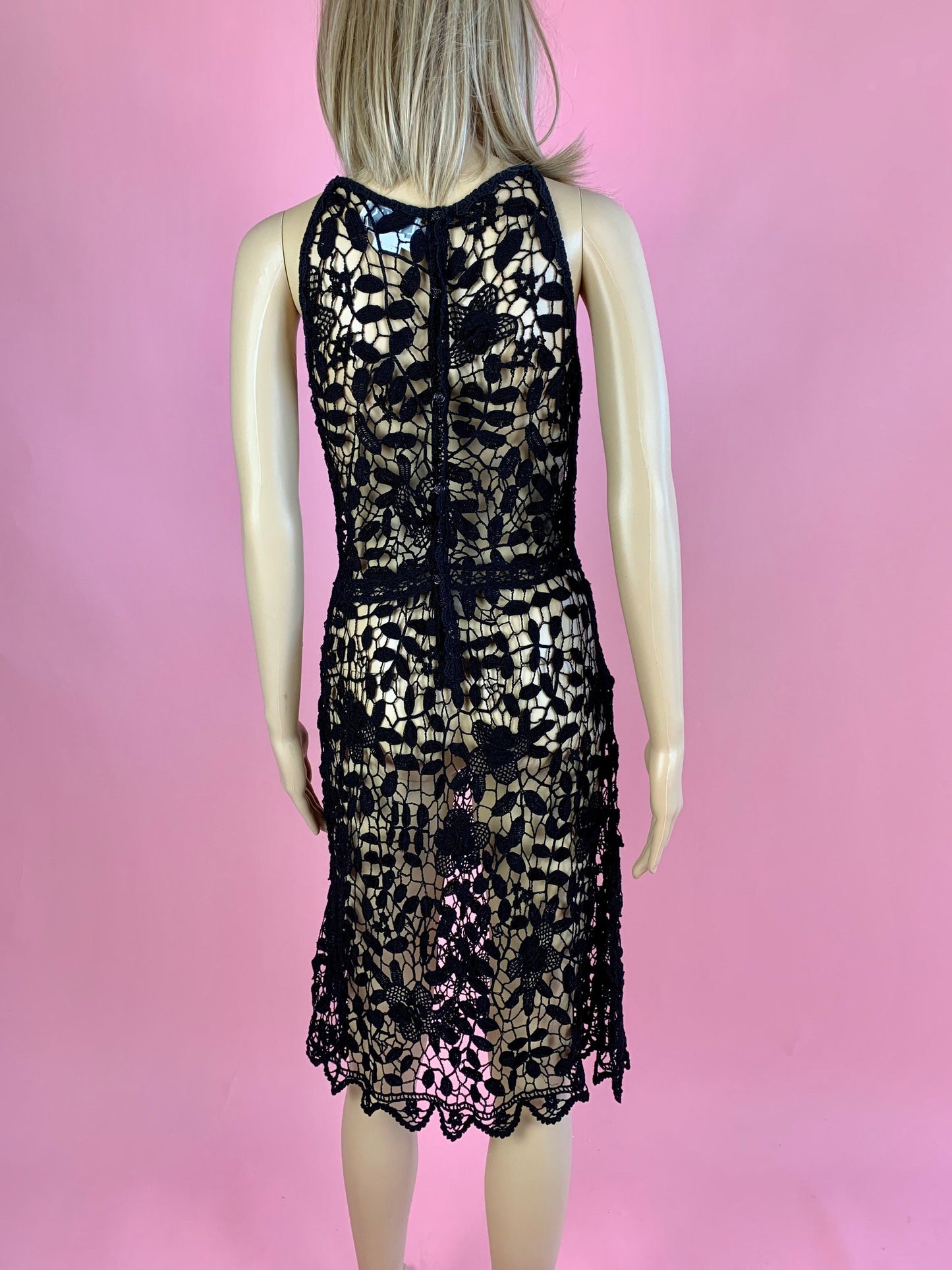 Back view. Lim's Vintage black crochet sleeveless halter midi dress with leaf and floral motif and zig-zag hem. The top is reversible and can be worn with buttons going down the front or back. Elastic waistband connects the top and bottom of the dress.