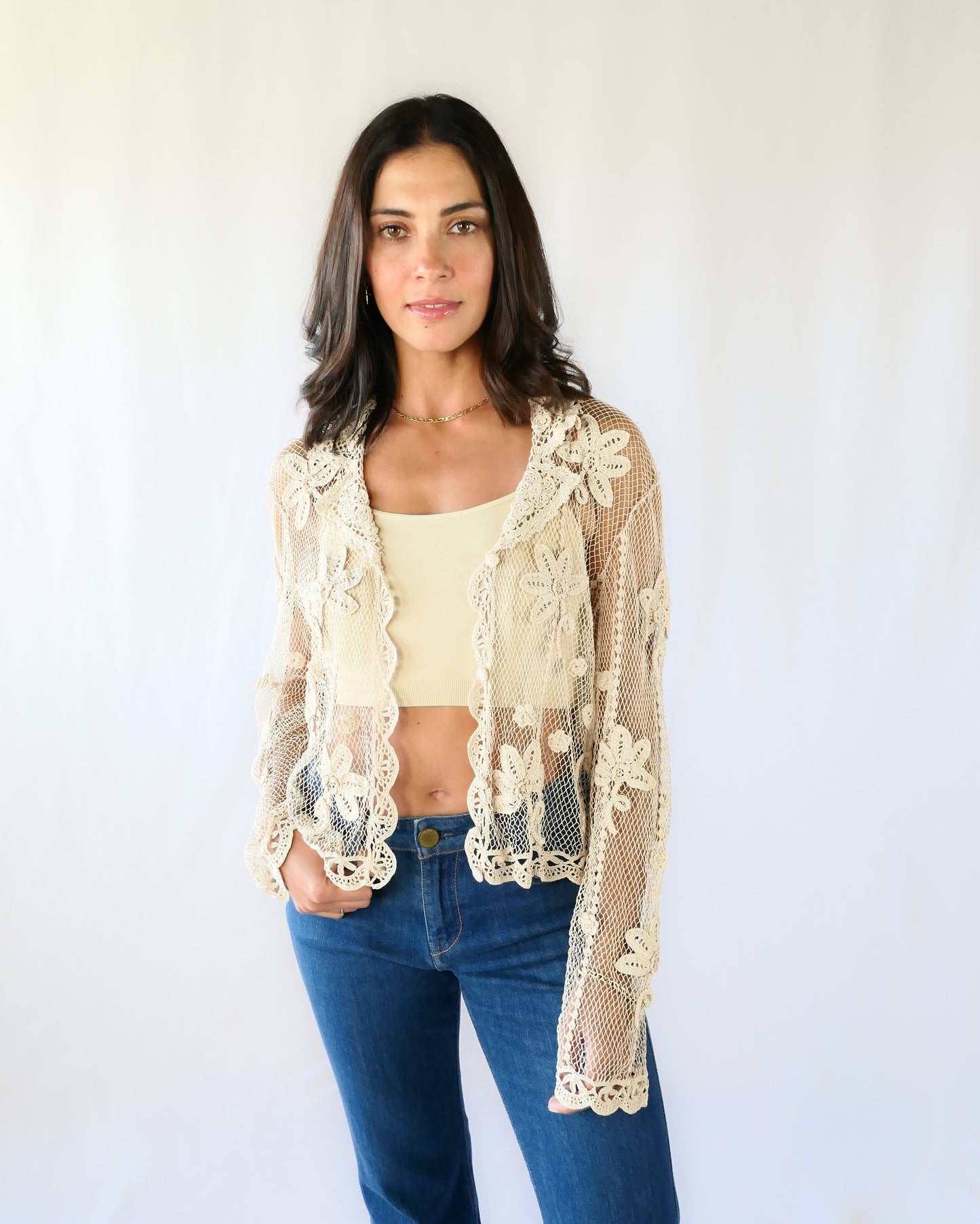 A sheer, hand crocheted Lim's Vintage original long sleeve cardigan with a wide notched collar and daisy floral motif design throughout. Pair it with a tank top, jeans, and boots or sandals for a fresh, boho chic look. Here the model wears the jacket unbuttoned.