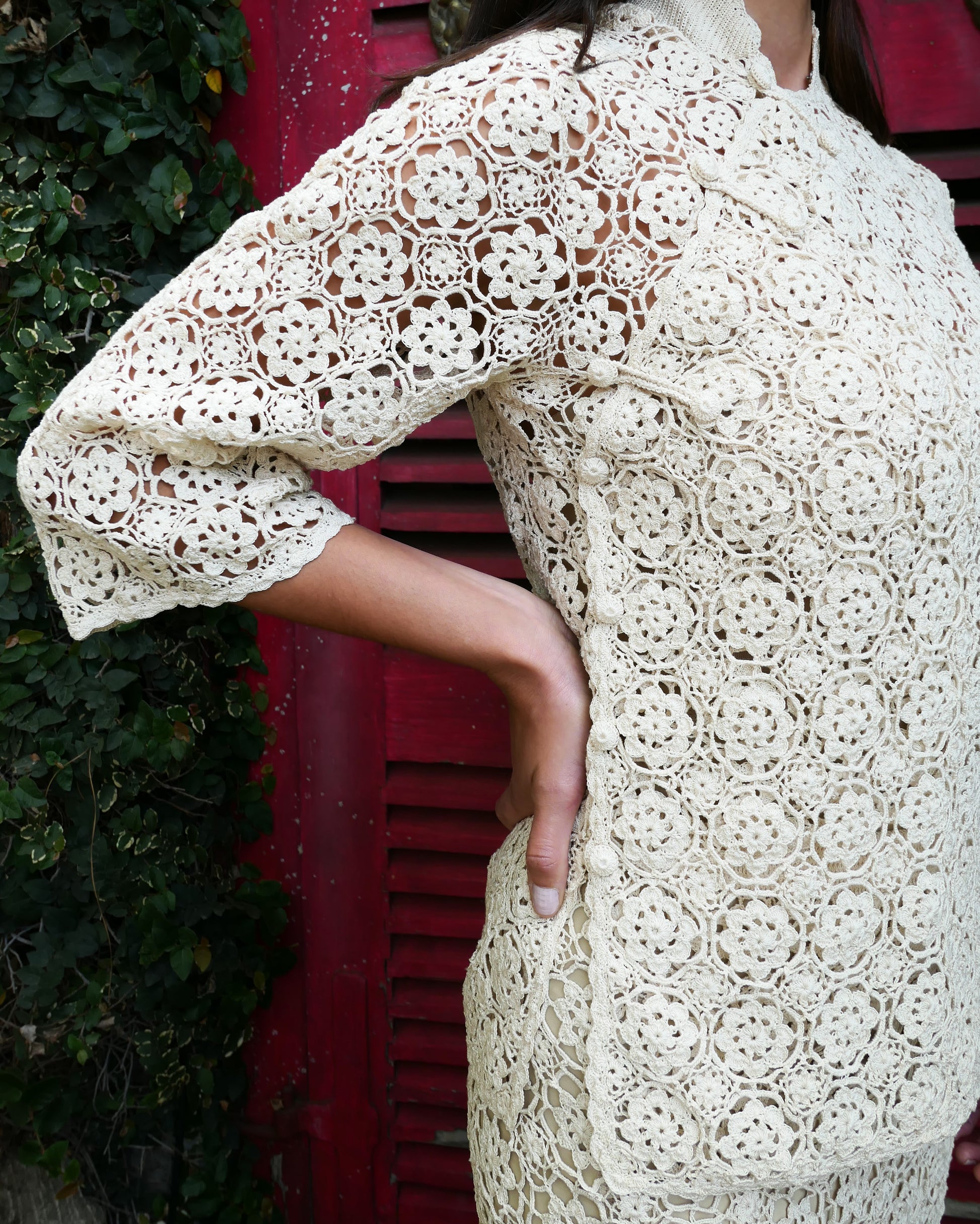 Closeup side view. An intricately hand crocheted top and skirt set reminiscent of the traditional Chinese Qipao, with its high mandarin collar, traditional knotted buttons that run along the front and side of the top, and the side slits that run up either side of the skirt. Simple, refined, beautiful, and one of our classic Lim's Vintage bestsellers. Color: Natural