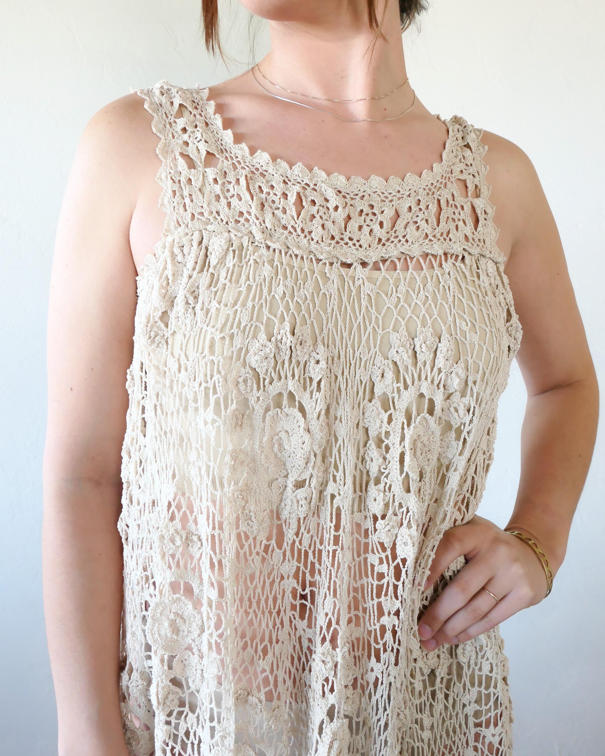 Closeup of front. A sleeveless babydoll dress made from our Lim's Vintage original fishnet crochet fabric with a repeating floral themed design throughout. A versatile, comfortable, fun-to-twirl-around-in pullover dress that you can wear wherever you go. The area above the breast and under the armpits is elastic and stretchable, making the dress suitable for most sizes. Size: One size fits most Color: Natural Material: 100% cotton