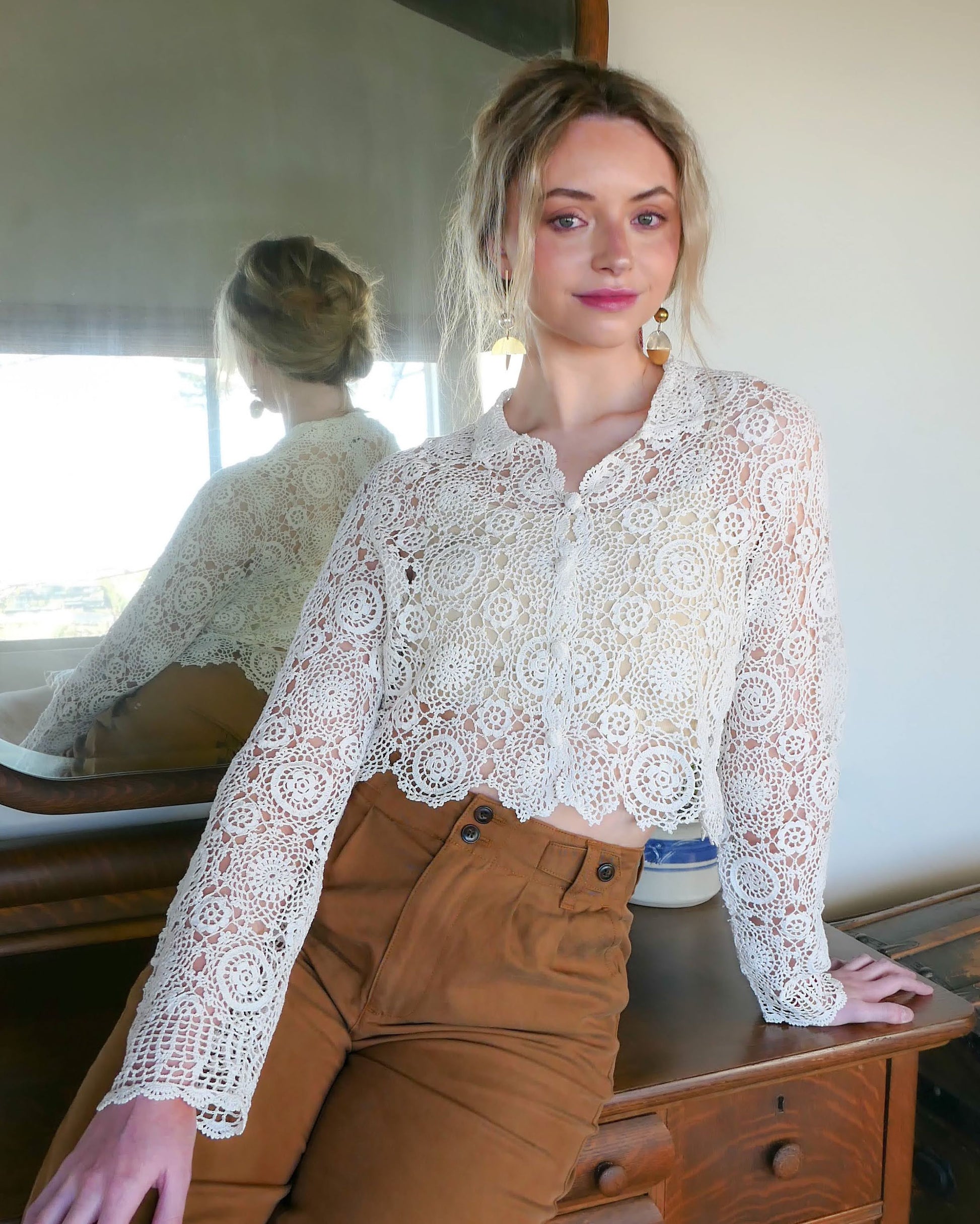 Mode is wearing ivory colored Lim's crochet top. A versatile and boho chic hand crocheted cropped cardigan sweater in Ivory with a unique, repeating kaleidoscope-like floral pattern throughout. Dress it down with a pair of jeans and sandals, or dress it up with neutral colored wide leg pants, heels, and a pair of vintage dangly earrings.  Size: Fits Small to Medium