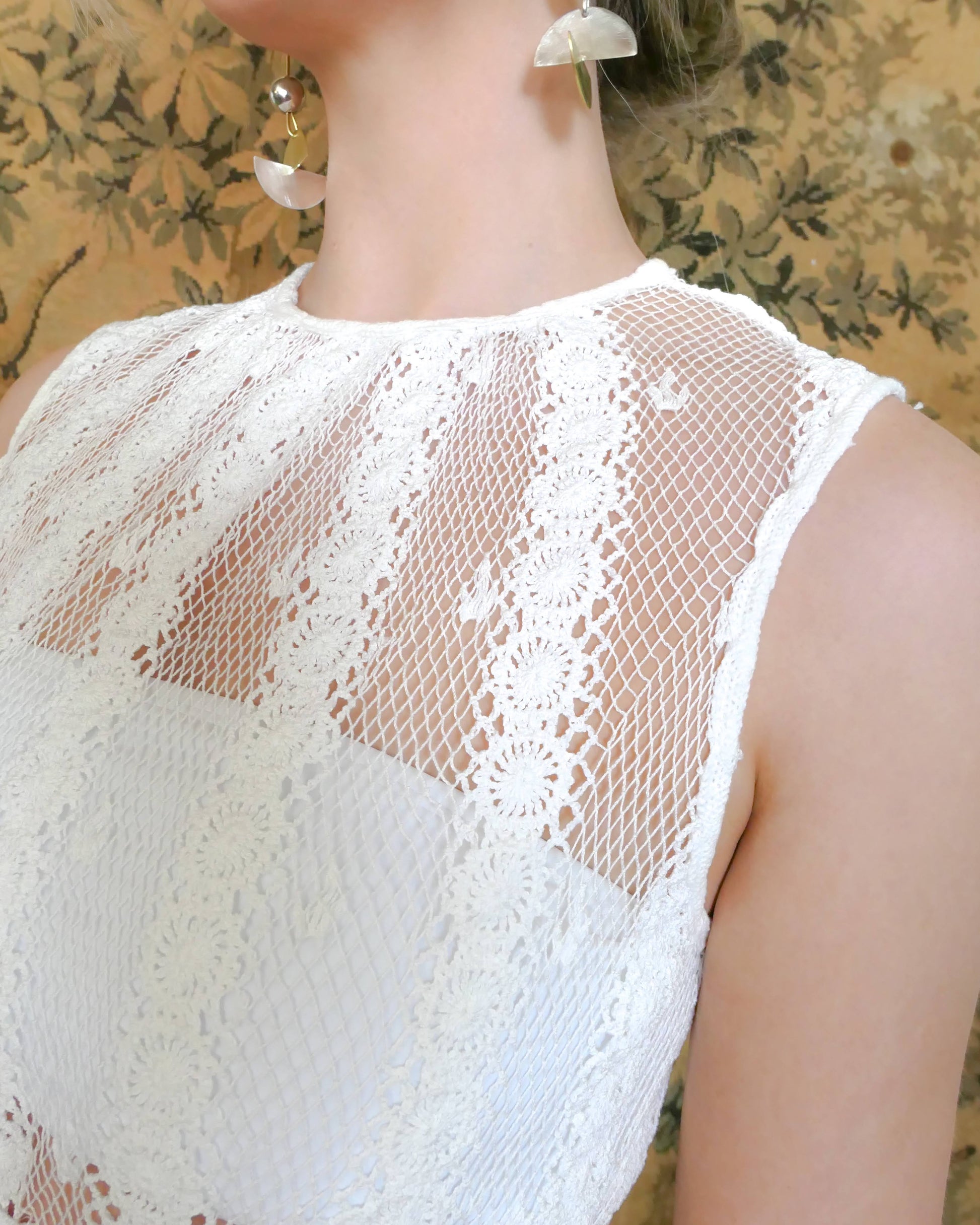 A delicate mesh crochet sleeveless midi dress in white using our vintage Lim's crochet fabric with a comfortable fitting, elastic high waist and vertical stripes composed of connected pinwheel-like circles.  The dress flares out gradually towards the two-tiered hem and is accented with a floral trim. This dress is versatile and can be worn as a vintage wedding or party dress, or thrown over your bikini and paired with a straw hat, it will make your beach day elegantly cool.  