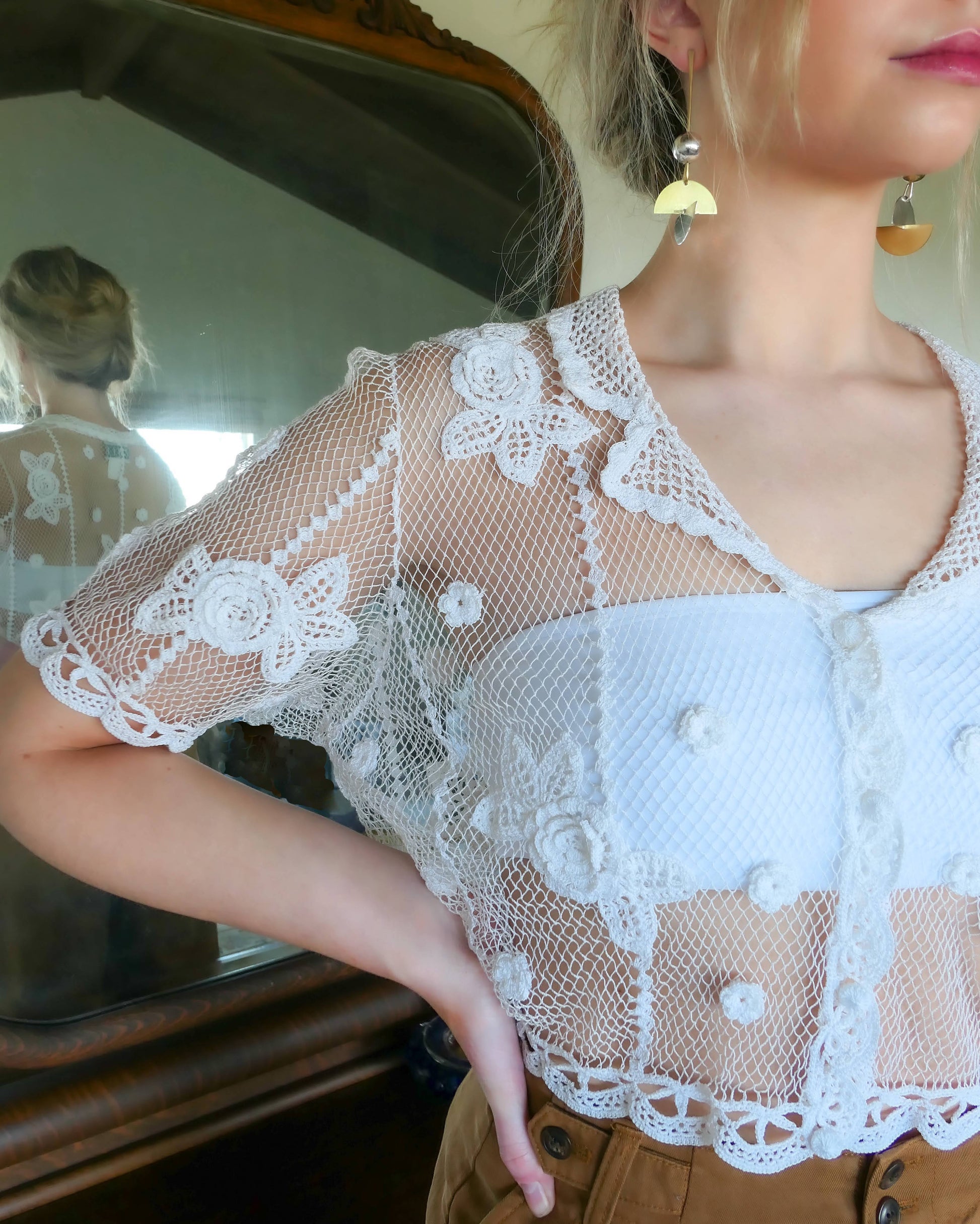 Closeup front view. Add a romantic twist to your wardrobe with this Lim' Vintage original 1990s hand crocheted short sleeve cardigan with a carnation flower motif and scalloped hem at the sleeves and waist.  The cardigan is stretchable and fits a range of sizes. 