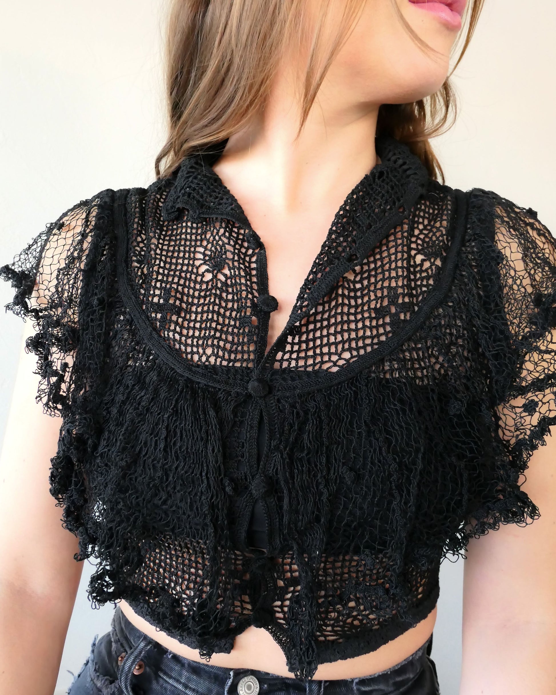 A super cool, super sassy hand crocheted fitted crop top in black with plenty of ruffles and frills for a fun, vintage inspired wardrobe.  Buttons up the front and crochet ruffles along the front covering the chest and over the shoulders. 