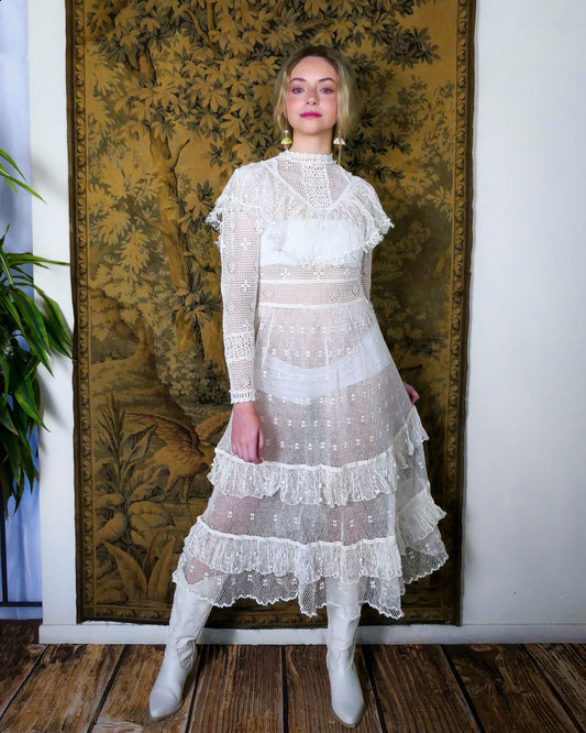 Lim's original hand crocheted maxi dress from the 1980s, worn by Jane Fonda and placed in a major fashion magazine ad. The dress is reversible and can be worn with the buttons going up the front or back of the dress.  Ruffle trim along the chest covering the breast area, and two tiered ruffle hem at the bottom of the dress.  Very sheer crochet dress, fitted at the waist, with a tie at the back.  Detailed crochet emellishment on the forearm, sleeve hem, and neckline.  Models is wearing white colored dress. 
