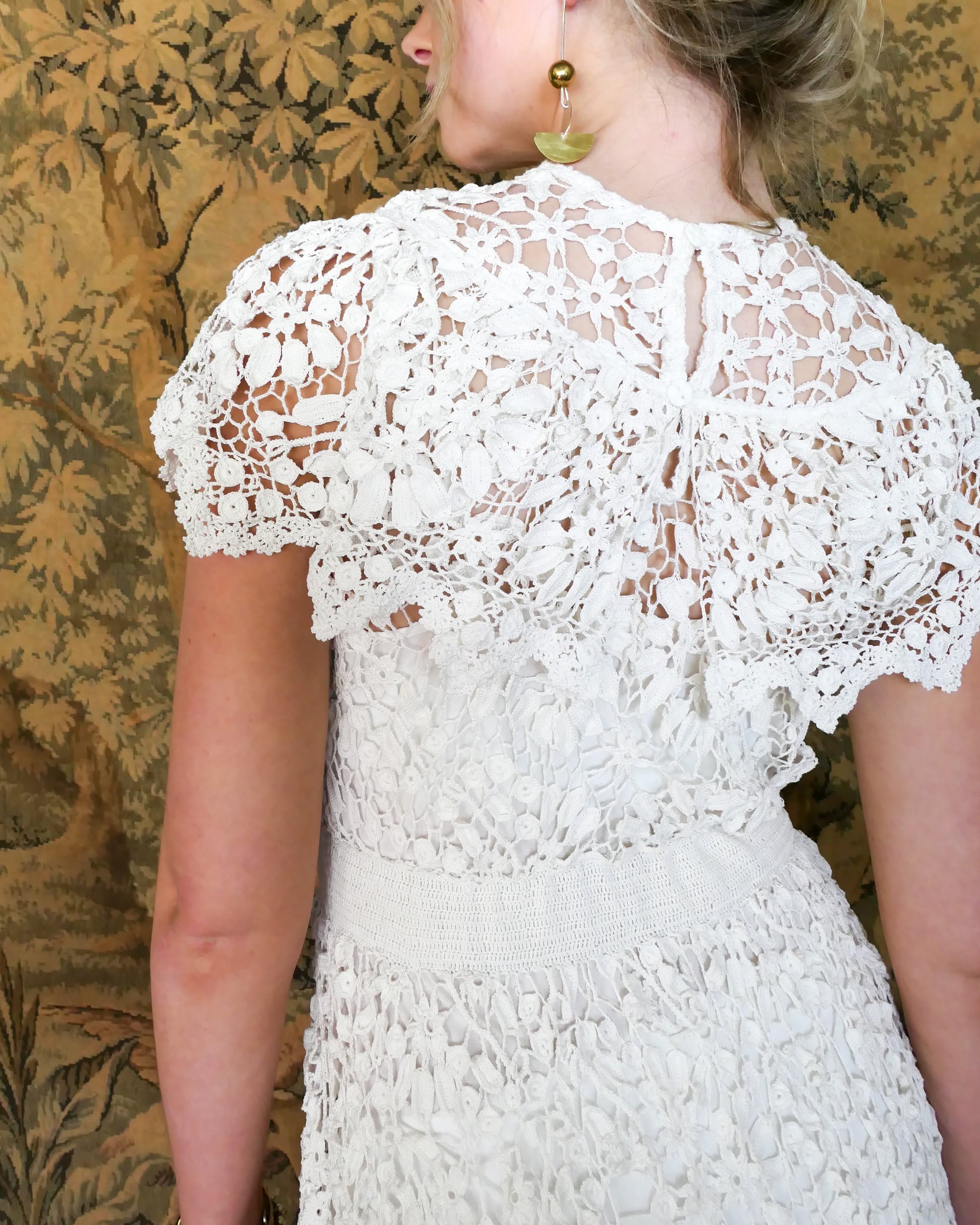 A romantic white crochet midi dress with a floral and leaf pattern, comfortable elastic waistband, and a flattering neck and shoulder design. Perfect as a vintage wedding dress or a special occasion! Wear with a white slip and heels for a refined, feminine look, or pair with boots for a more casual outing.