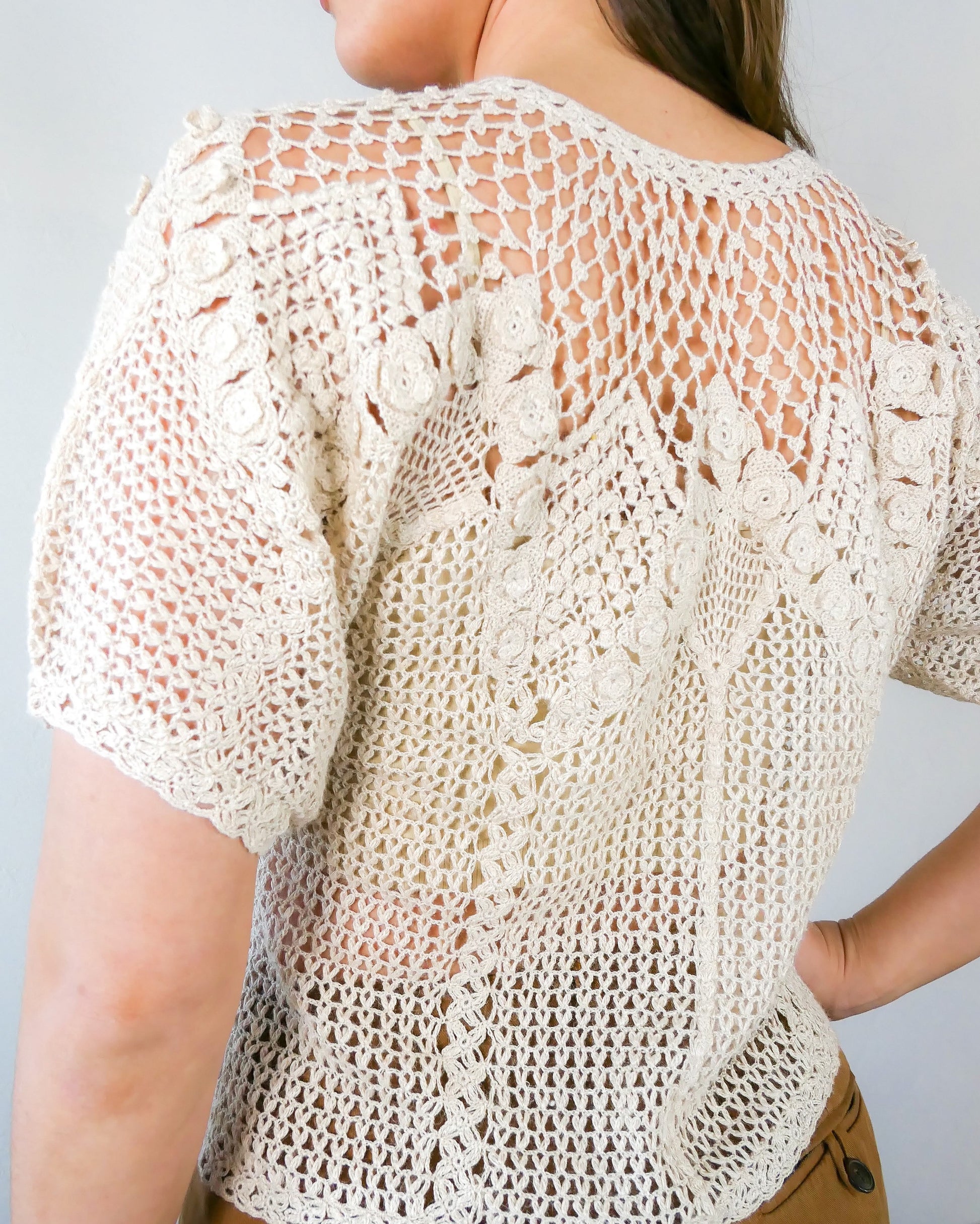 A classic Lim's Vintage hand crocheted button down top with a beautiful zig zag pattern on both the front and back, with lighter stitching around the chest and shoulders to bring a sense of lightness and space to the neckline. Petite flower buds sprout up from and accent the edges of the zig zag. This natural color top is versatile, comfortable, and adds a beautiful vintage accent to your wardrobe.